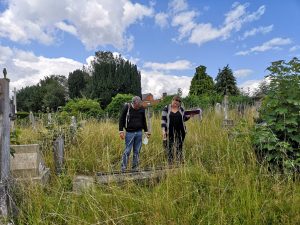 two people standing by a headstone in a graveyard